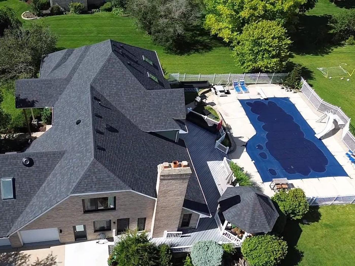 Drone view of a large brick home in New Lenox with a new dark roof, gazebo and pool
